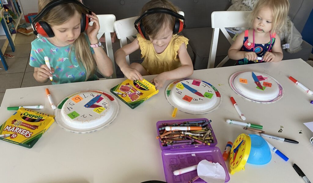 three homeschool students sitting at table learning to tell time with homemade paper plate clocks