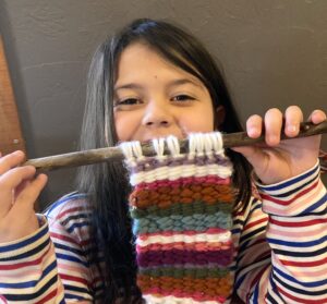 Girl learning how to knit with a striped knitting project