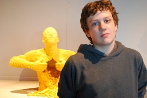 Student in front of a yellow lego sculpture of a person pulling open their chest.
