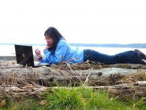 Student laying alongside the water, using a laptop computer