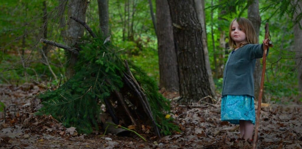 Child standing guard by tee pee made of pine branches