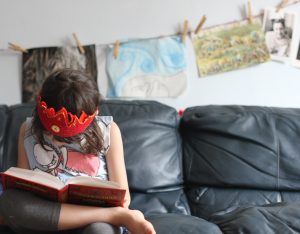 girl with crown on couch reading