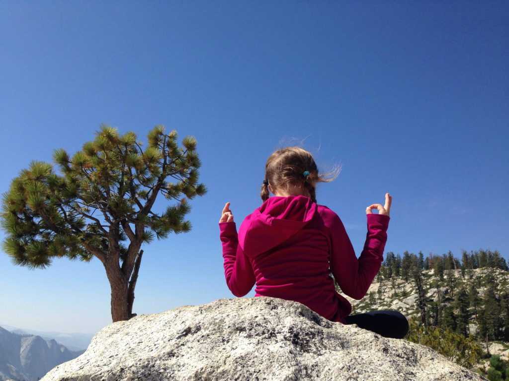 Oak Meadow girl sitting on rock meditating