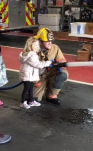 young girl spraying hose with help of firefighter