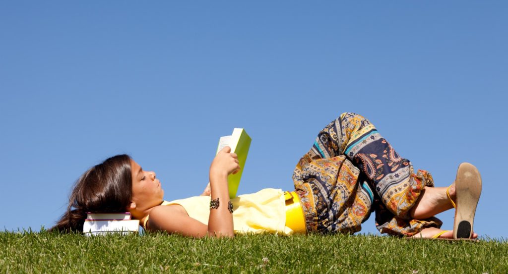 Oak Meadow student lying on the grass reading a book