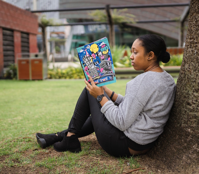 Student sitting by tree reading on college campus