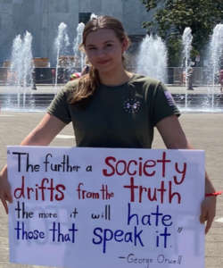 Jillian Bauer holding Sign that says "The Further a society drifts from the truth the more it will hate those that speak it" - George Orwell