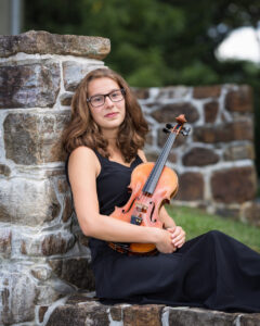 Megan Frederick sitting on a stone wall with her Violin