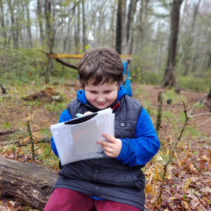 homeschool student sitting on a log and journaling