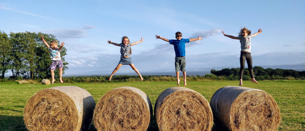 homeschool students jumping for joy on haybales
